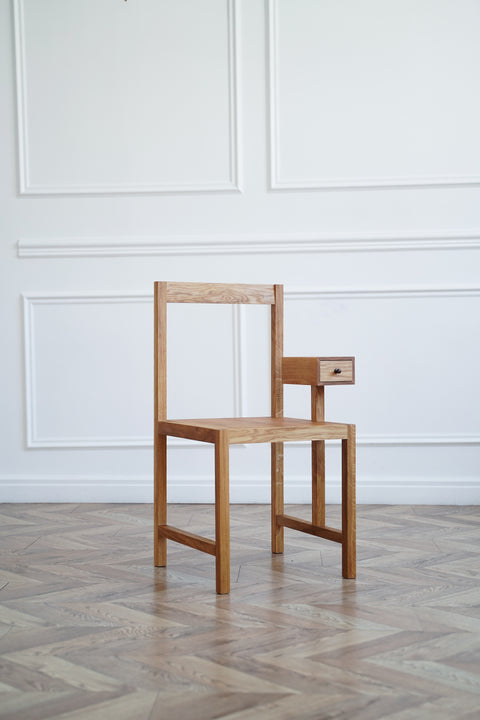 Wooden chair with a drawer against a white paneled wall