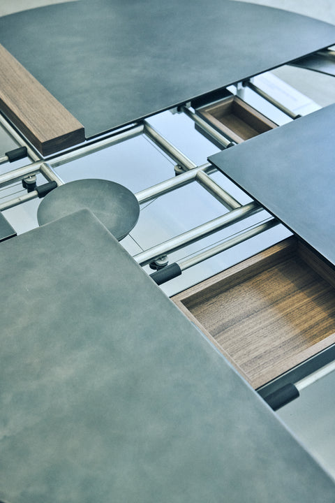 Close-up of a modern round table with multiple surfaces connected by metal tubes and a wooden drawer